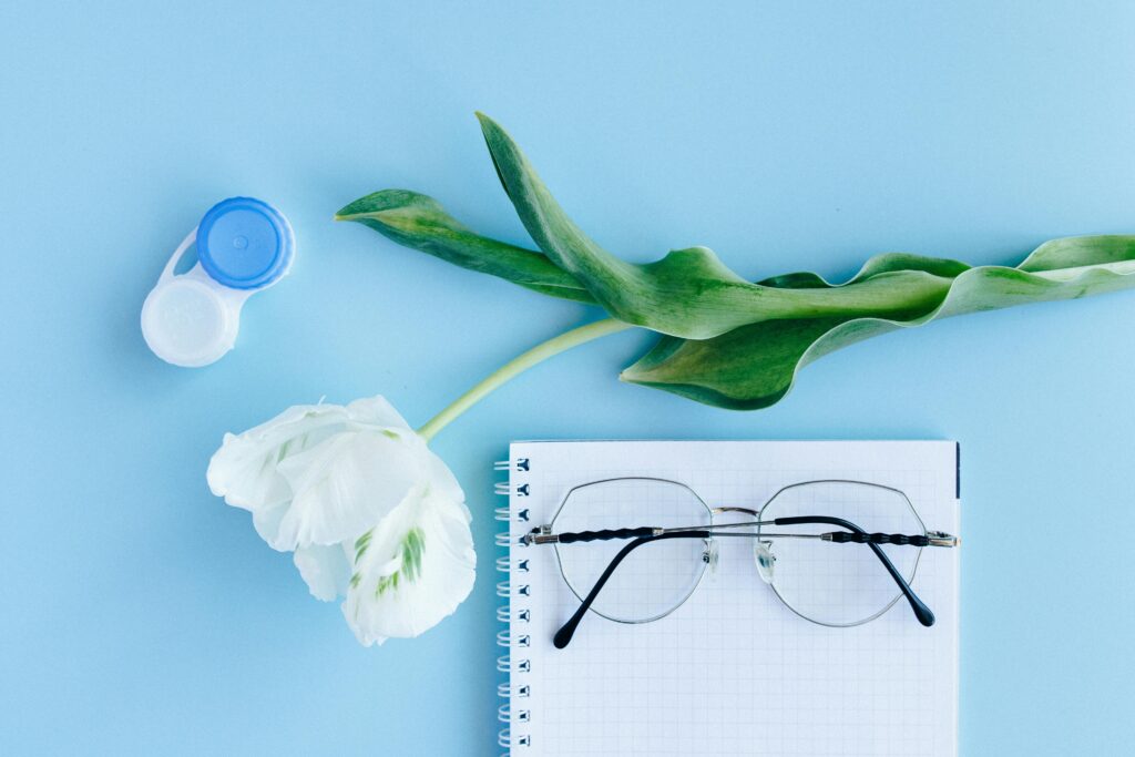 Aesthetic composition with glasses, tulip, and contact lens case on blue background.