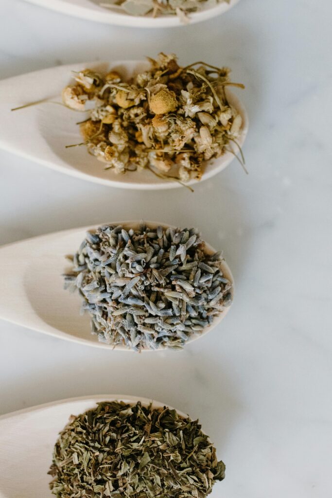 Flat lay of wooden spoons with chamomile, lavender, and dried herbs for aromatherapy and cooking.