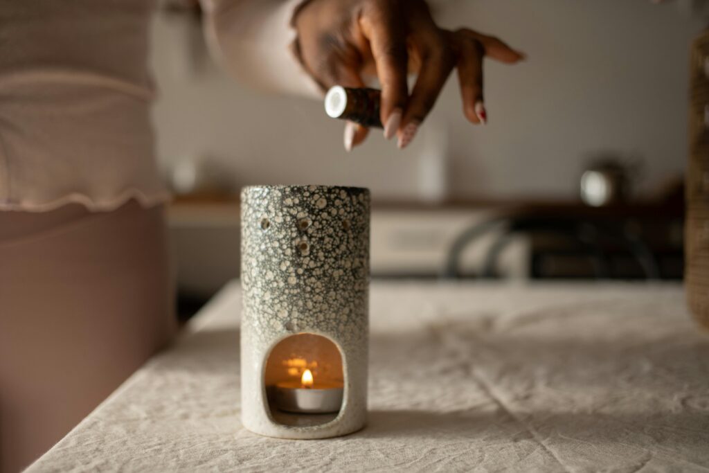 A close-up of a hand pouring essential oil into a diffuser with a lit candle inside, creating a warm ambiance.